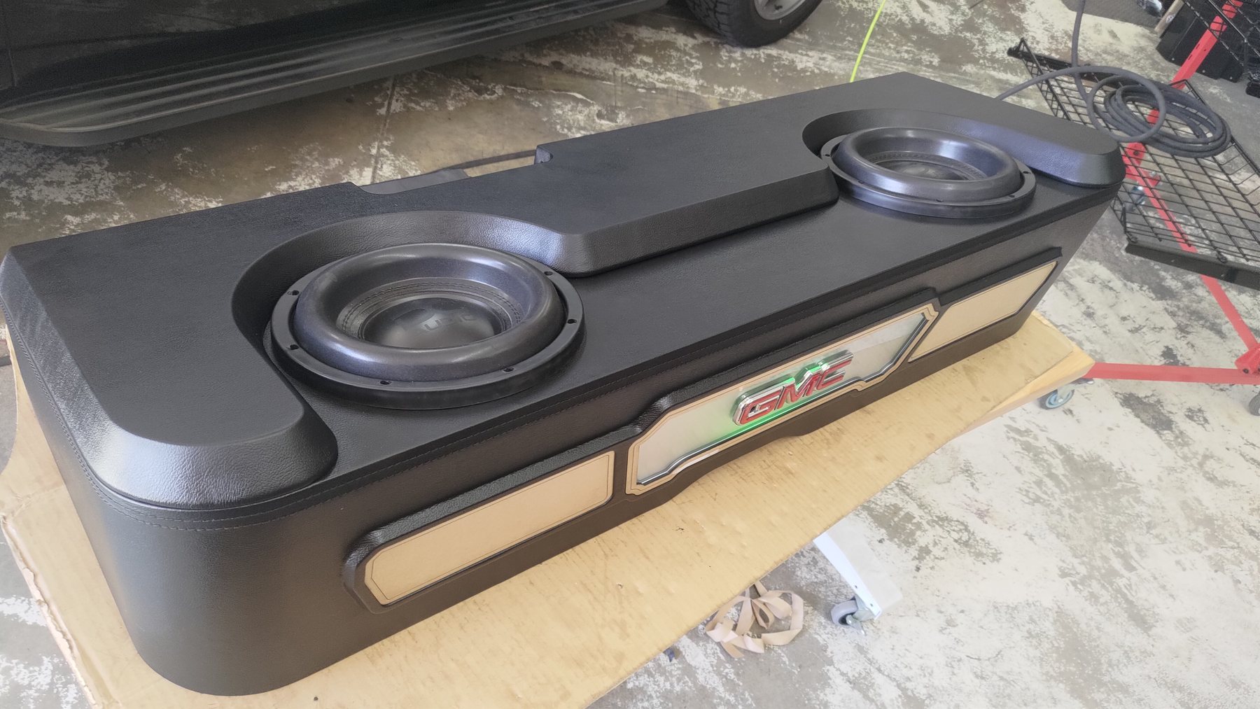 Two subwoofers mounted in a finished black enclosure on a workbench