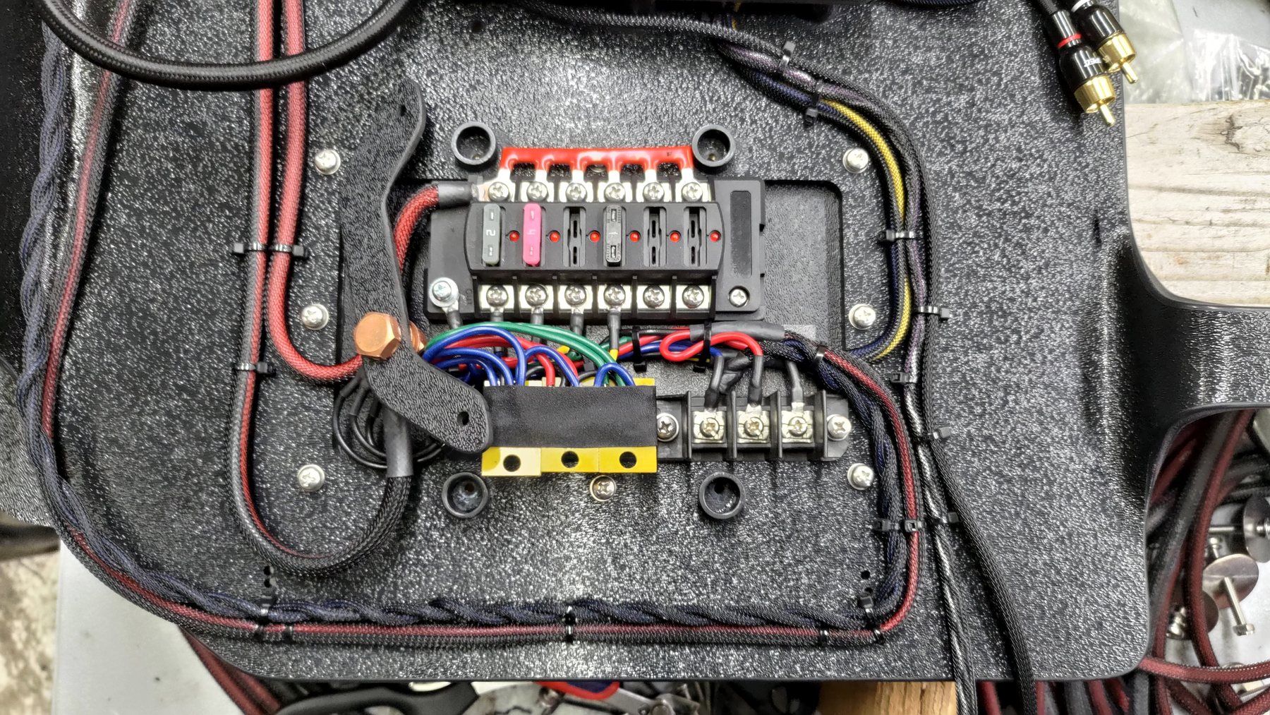 Fused distribution block mounted on a carpeted panel with routed power cables